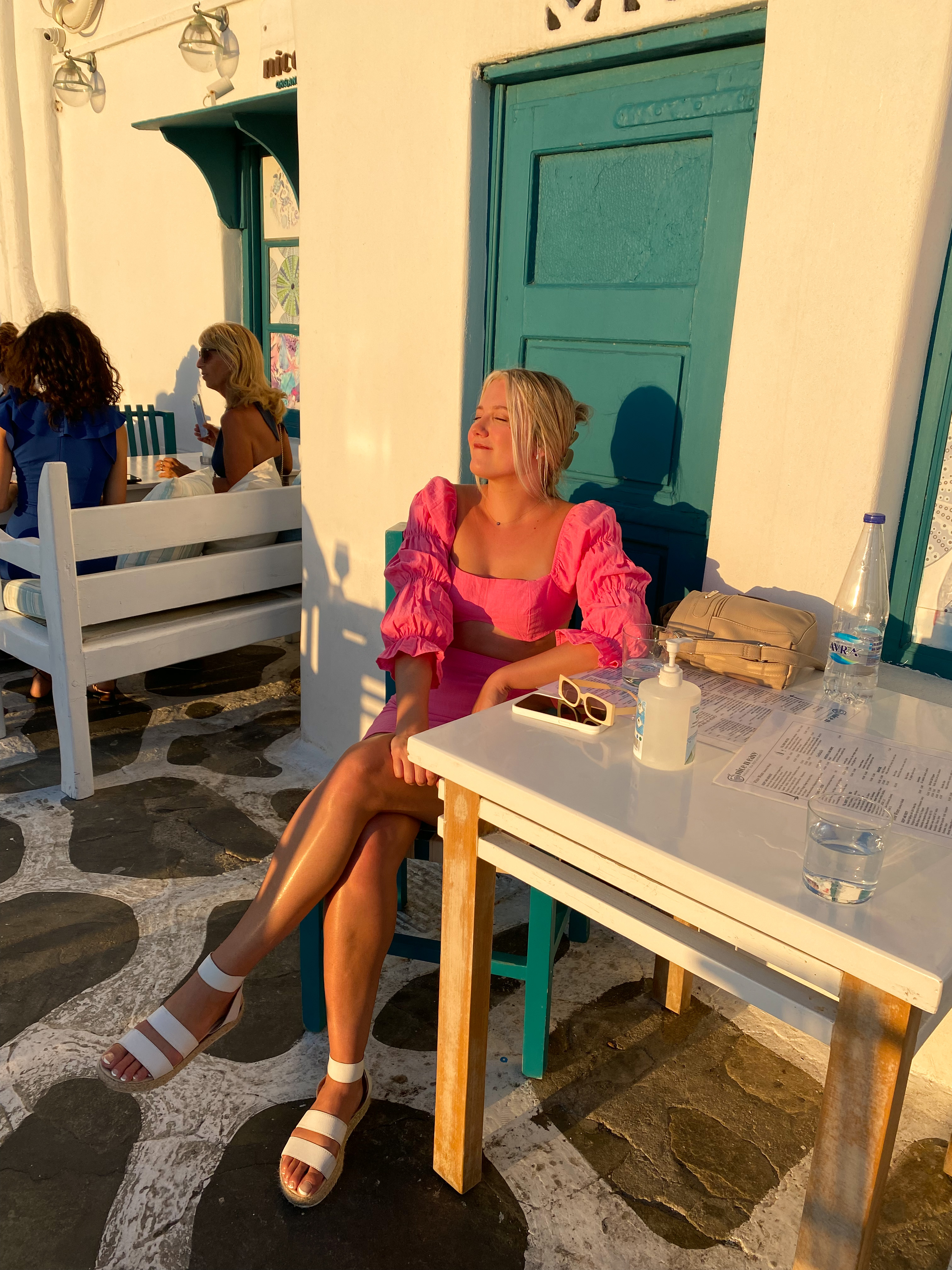 Blonde in bright pink two piece top posing by sunset in Mykonos Greece